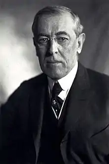 Half-length portrait of a man wearing a three-piece suit, a necktie, round-rimmed glasses and looking directly towards the photographer with an emotionless expression.